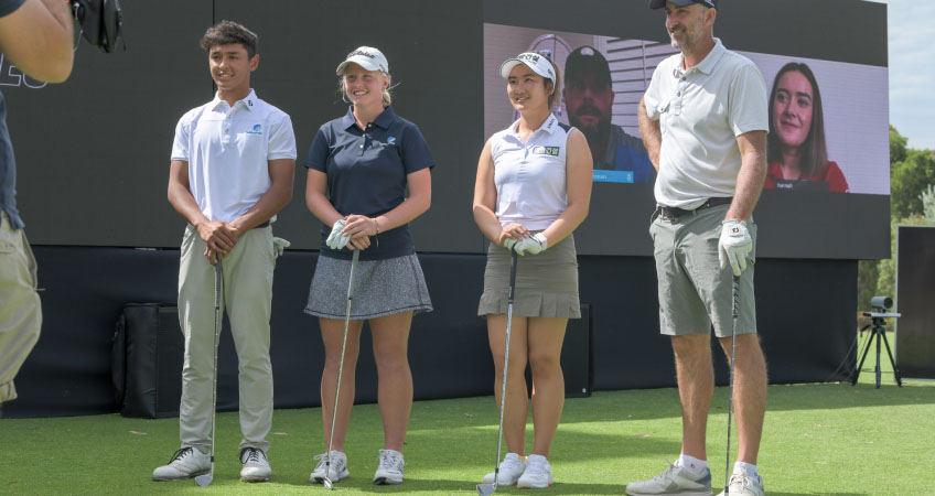 Four smiling golfers stand together with their clubs while two people who have video conferenced in look on.