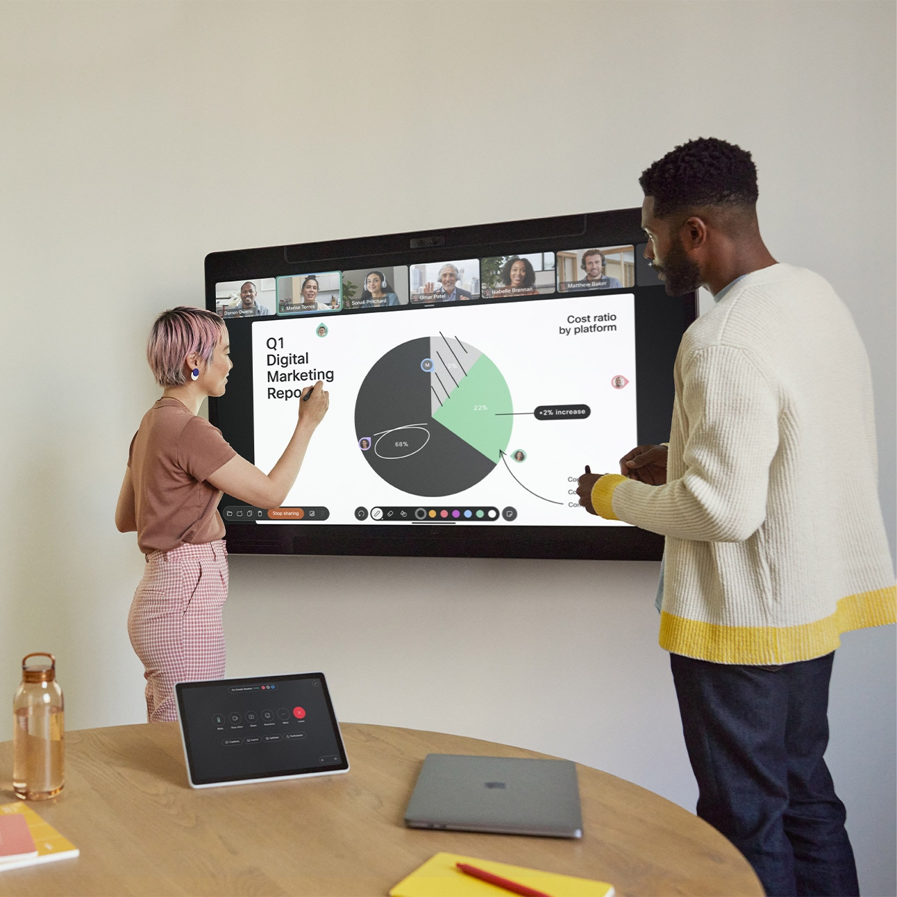 Two people collaborating and brainstorming in a small meeting room with the Cisco Board Pro mounted on the wall and the tabletop Cisco Room Navigator. Both persons hold a board pen and one of them is actively annotating on the digital whiteboard screen showing a pie chart, notes, arrows, and the live video of remote meeting participants.